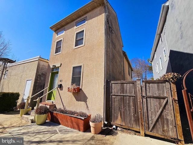 rear view of property featuring entry steps, a gate, and stucco siding