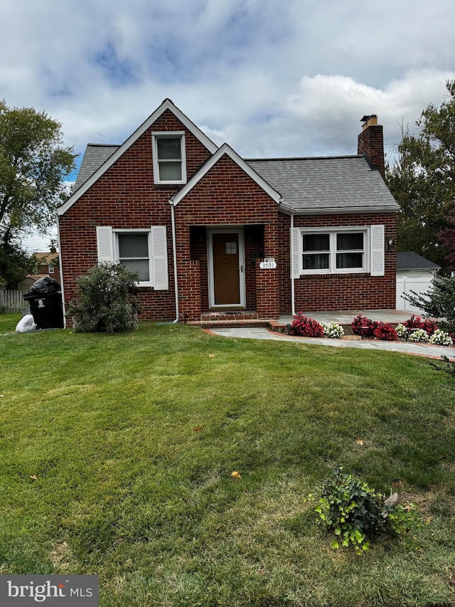 view of front of house with brick siding, a chimney, a front yard, and a shingled roof