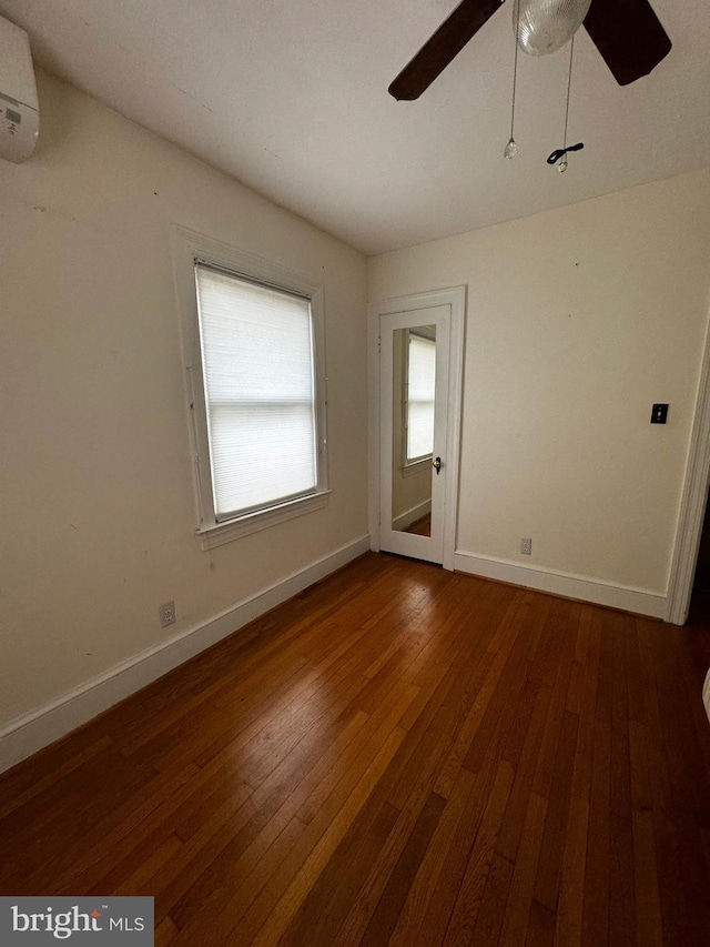 empty room featuring dark wood finished floors, baseboards, a wall mounted air conditioner, and ceiling fan