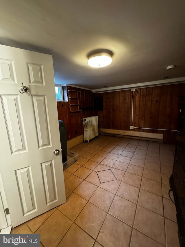 kitchen with a baseboard radiator, radiator, light tile patterned flooring, and wood walls