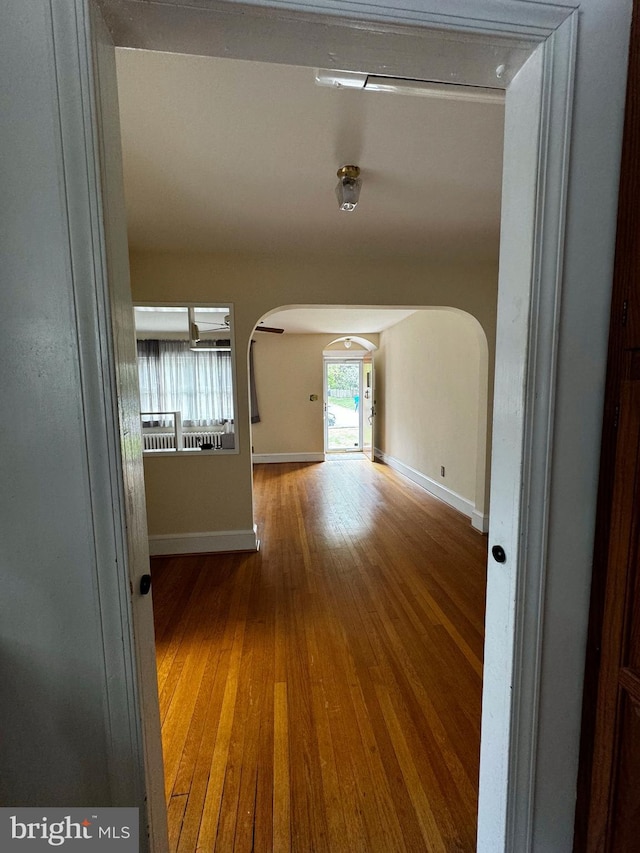 hallway featuring baseboards, arched walkways, and wood finished floors