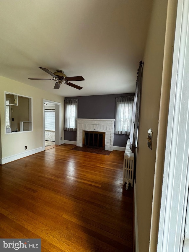 unfurnished living room with radiator, baseboards, a ceiling fan, and wood finished floors