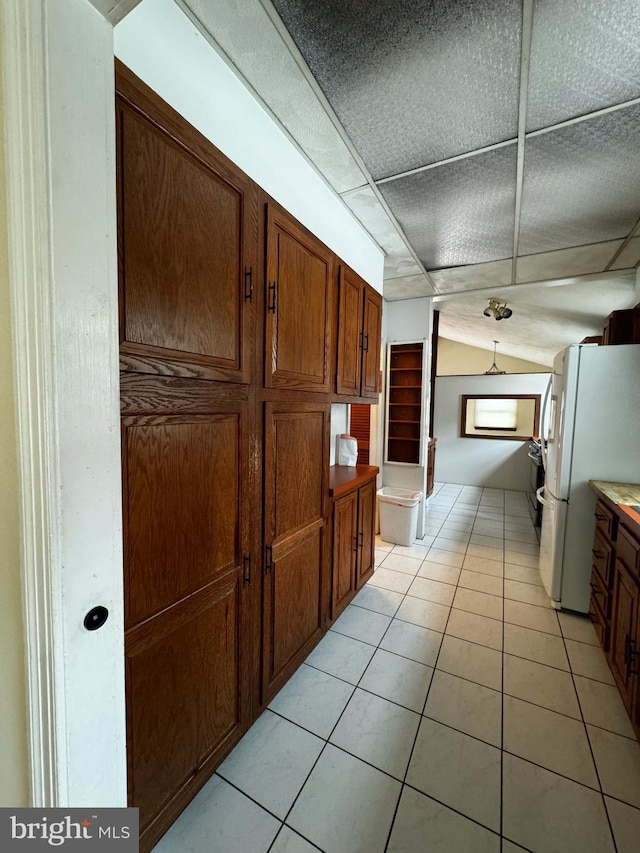 kitchen with lofted ceiling, light tile patterned flooring, brown cabinets, and freestanding refrigerator