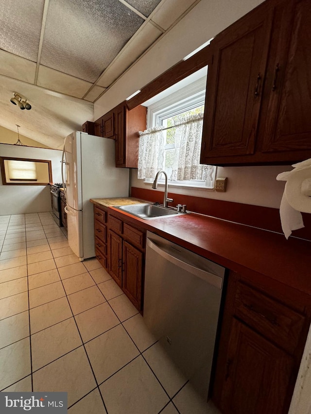 kitchen featuring lofted ceiling, light tile patterned floors, stainless steel dishwasher, freestanding refrigerator, and a sink