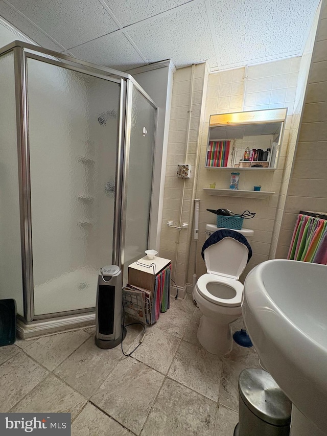 bathroom featuring toilet, a stall shower, a drop ceiling, and a sink