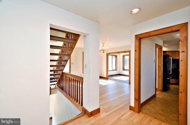 hallway featuring light wood-type flooring, an upstairs landing, recessed lighting, an inviting chandelier, and baseboards