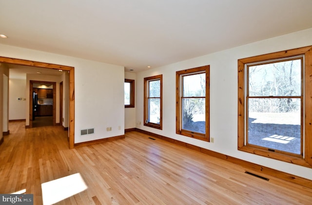 spare room featuring light wood finished floors, visible vents, and baseboards