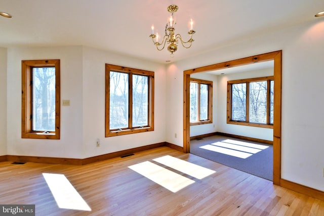 empty room with light wood-style flooring, a notable chandelier, baseboards, and visible vents