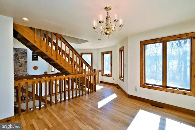 stairs featuring an inviting chandelier, wood finished floors, baseboards, and visible vents