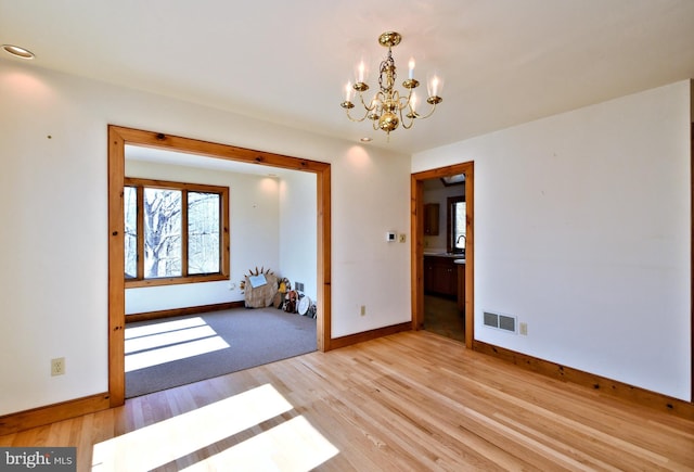 unfurnished room featuring a notable chandelier, baseboards, visible vents, and light wood finished floors