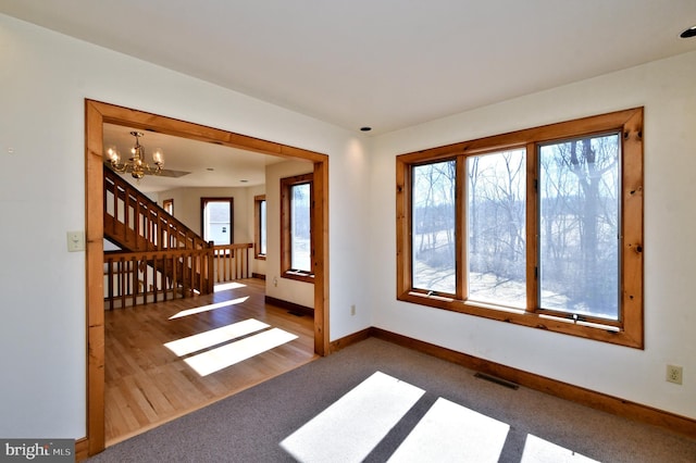 carpeted empty room with visible vents, a healthy amount of sunlight, baseboards, and an inviting chandelier