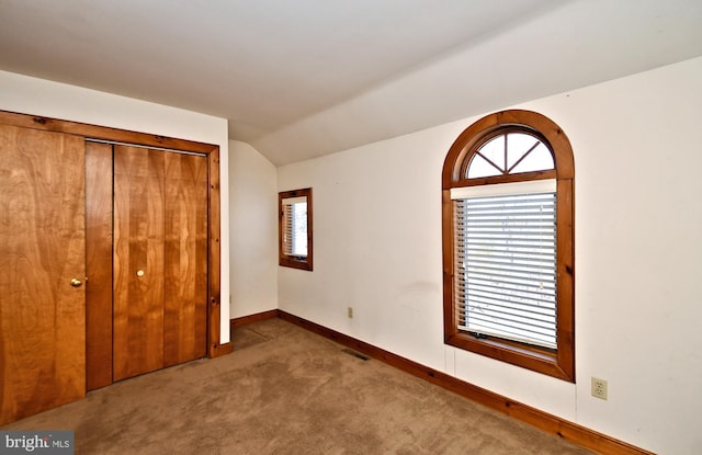 unfurnished bedroom featuring visible vents, a closet, carpet floors, baseboards, and vaulted ceiling