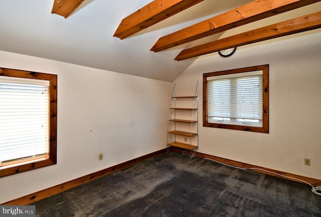 spare room featuring lofted ceiling with beams, baseboards, and dark colored carpet