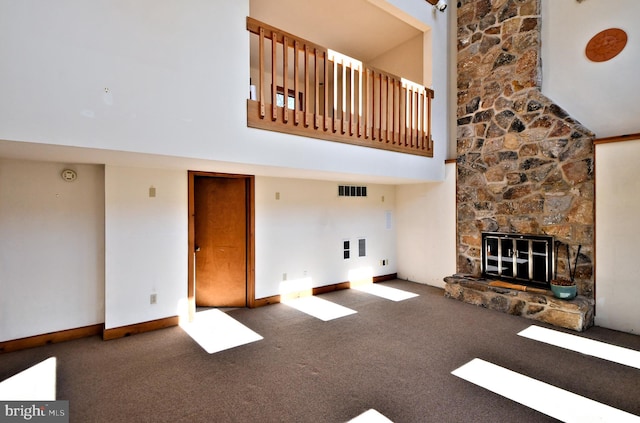 unfurnished living room featuring a stone fireplace, visible vents, carpet, and a high ceiling