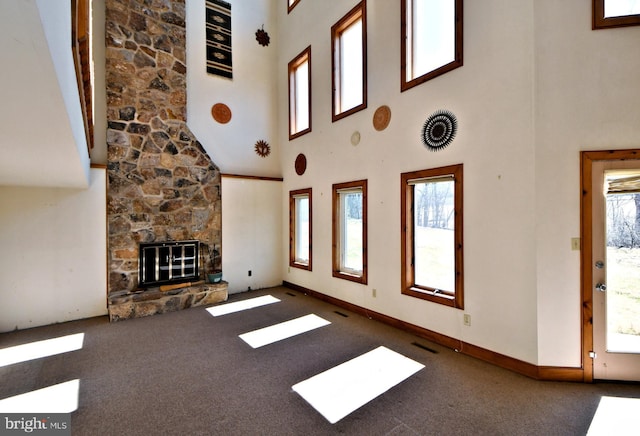 unfurnished living room with visible vents, baseboards, a stone fireplace, and carpet flooring