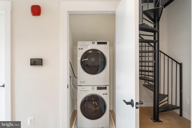 laundry room featuring stacked washer / drying machine, wood finished floors, and laundry area