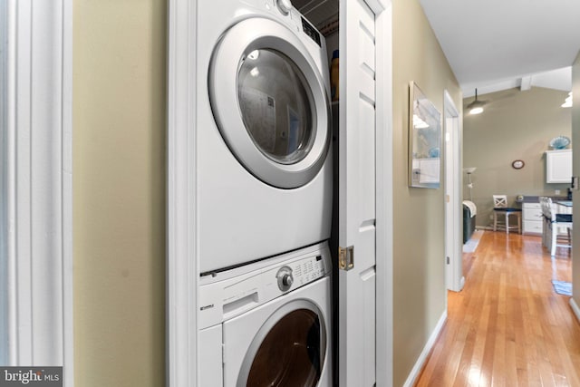 laundry room featuring laundry area, stacked washer and clothes dryer, baseboards, and light wood-style floors