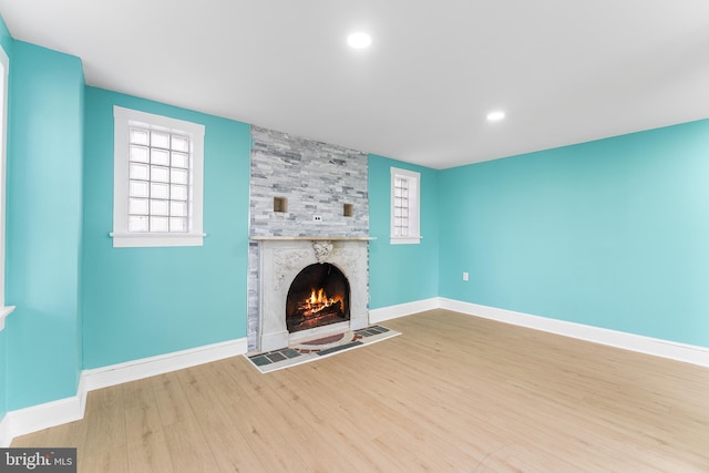 unfurnished living room featuring plenty of natural light, a fireplace, baseboards, and wood finished floors