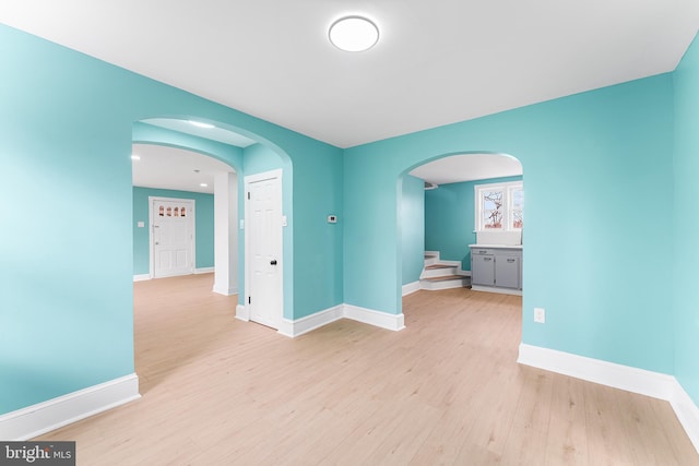 unfurnished room featuring baseboards, arched walkways, and light wood-style flooring