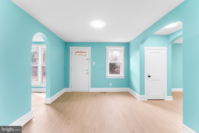 entrance foyer featuring baseboards, arched walkways, and wood finished floors