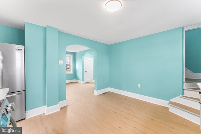 unfurnished living room featuring baseboards, arched walkways, and light wood-type flooring