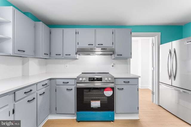 kitchen featuring under cabinet range hood, open shelves, stainless steel range with electric cooktop, freestanding refrigerator, and light countertops