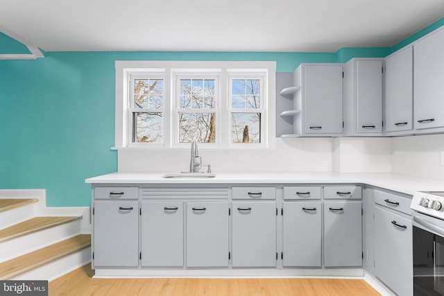 kitchen with a sink, light countertops, light wood-style floors, electric range, and open shelves