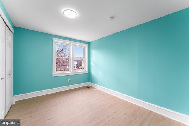 unfurnished bedroom with a closet, baseboards, visible vents, and wood finished floors