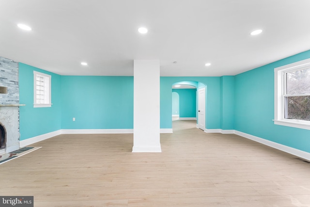 interior space featuring a fireplace, arched walkways, light wood finished floors, and baseboards