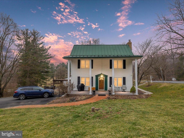 greek revival inspired property with a standing seam roof, a yard, covered porch, a chimney, and metal roof