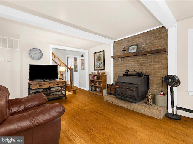 living area with visible vents, a wood stove, wood finished floors, baseboards, and stairs