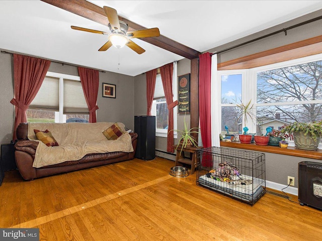 living area with baseboard heating, a healthy amount of sunlight, a ceiling fan, and wood finished floors