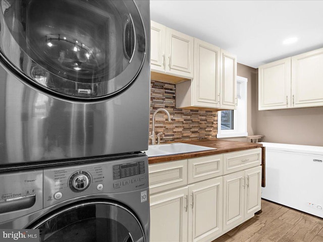 washroom featuring light wood-type flooring, cabinet space, stacked washer and clothes dryer, and a sink