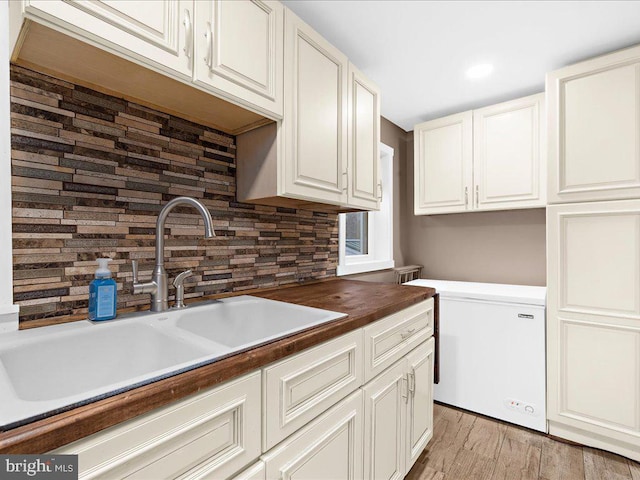 kitchen with backsplash, light wood-type flooring, white cabinetry, fridge, and a sink