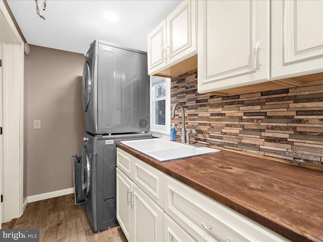 clothes washing area with baseboards, stacked washing maching and dryer, wood finished floors, cabinet space, and a sink