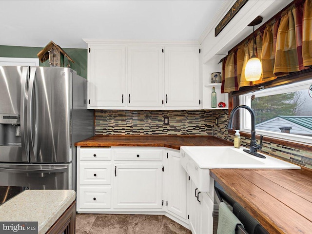 kitchen with open shelves, wood counters, stainless steel fridge, and backsplash