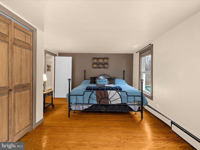 bedroom with light wood finished floors, baseboards, and a baseboard radiator