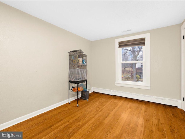 unfurnished room featuring visible vents, wood finished floors, baseboards, and a baseboard radiator