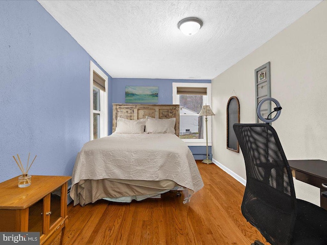 bedroom featuring a baseboard radiator, baseboards, a textured ceiling, and wood finished floors