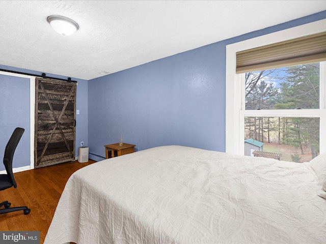 bedroom featuring a barn door, wood finished floors, baseboard heating, and a textured ceiling