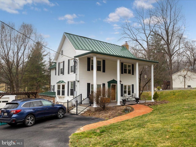 greek revival inspired property featuring a standing seam roof, a front lawn, metal roof, and a chimney