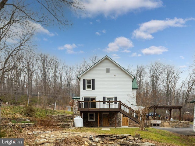 rear view of property featuring a detached carport, stone siding, stairs, and a deck