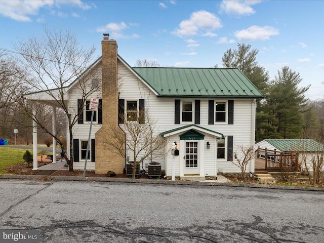 view of front of property with a wooden deck, central AC unit, a chimney, metal roof, and a standing seam roof