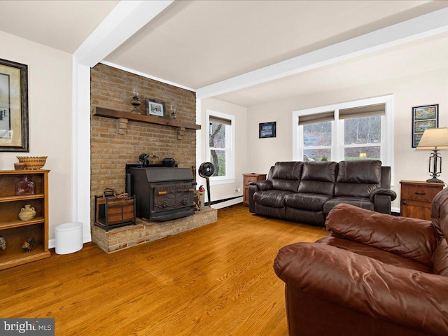 living room with a baseboard heating unit, beam ceiling, light wood-style flooring, and a wood stove