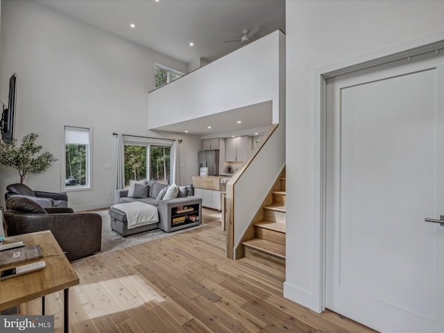 living room with recessed lighting, stairway, light wood-style flooring, and a high ceiling