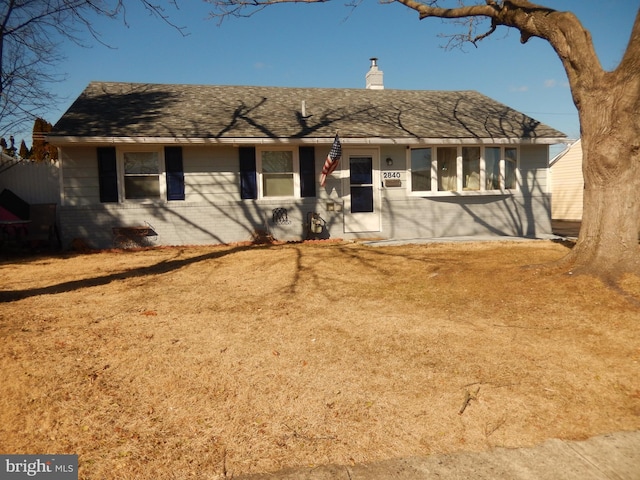 ranch-style house with a shingled roof, brick siding, and a chimney