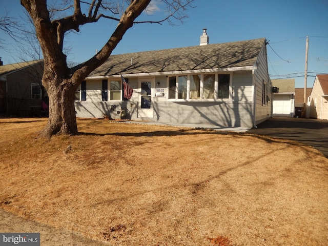 ranch-style home with an outbuilding, brick siding, a chimney, and a shingled roof