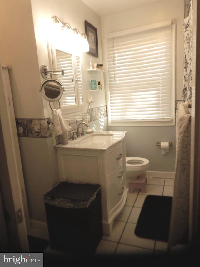 bathroom with tile patterned flooring, a healthy amount of sunlight, toilet, and vanity