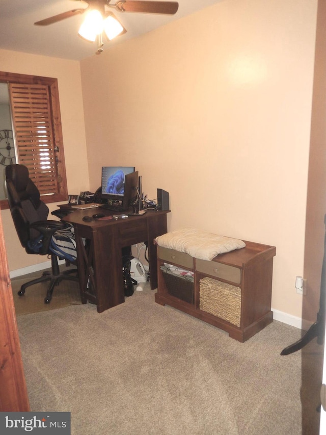 carpeted office space featuring a ceiling fan and baseboards