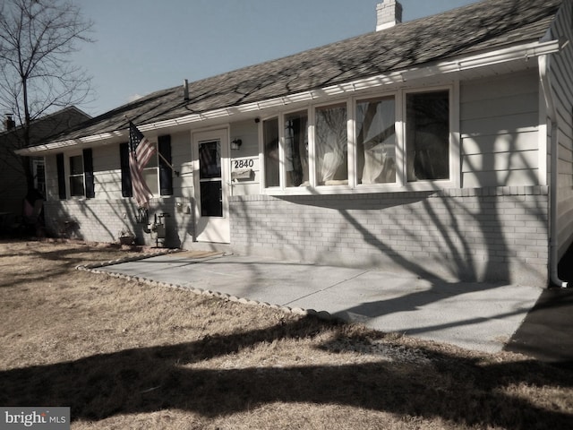 view of front of house with brick siding, a chimney, and a shingled roof